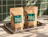Two brown kraft paper pouches printed with green 'Relax Coffee' labels placed on a metal tray with coffee beans in front of green tiles