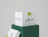 Stack of white eco mailer boxes with a one-colour black logo print, displayed on a green stand