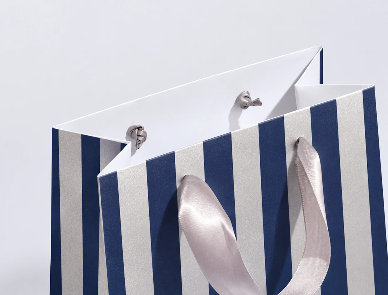 Close-up of a blue and white striped paper gift bag with grey satin ribbon handles