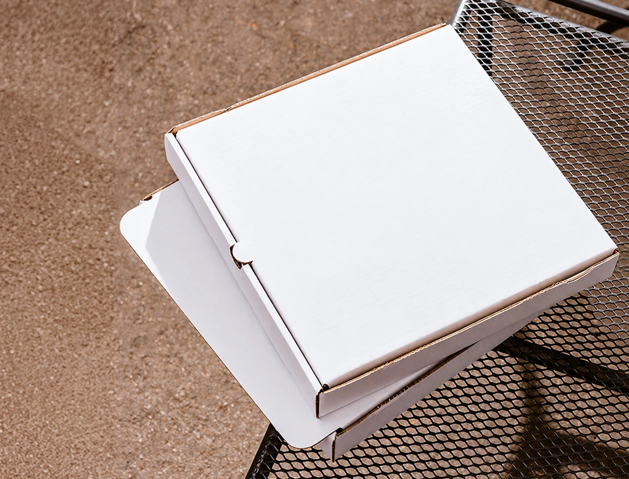 Top-down view of two plain white cardboard pizza boxes stacked on a outdoor metal mesh table