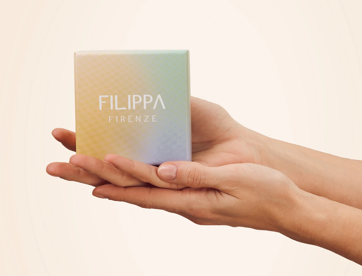 Two hands gently holding a small pastel gradient box printed with 'FILIPPA FIRENZE'