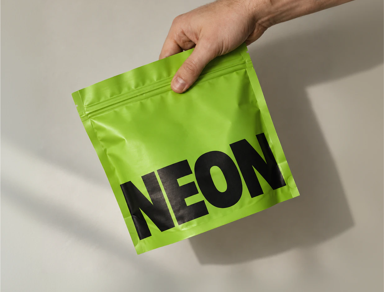 A hand holding a vibrant neon green ziplock pouch printed with bold black 'NEON' typography
