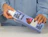 Hands holding a lilac printed product box with a tuck end, taking out a bottle