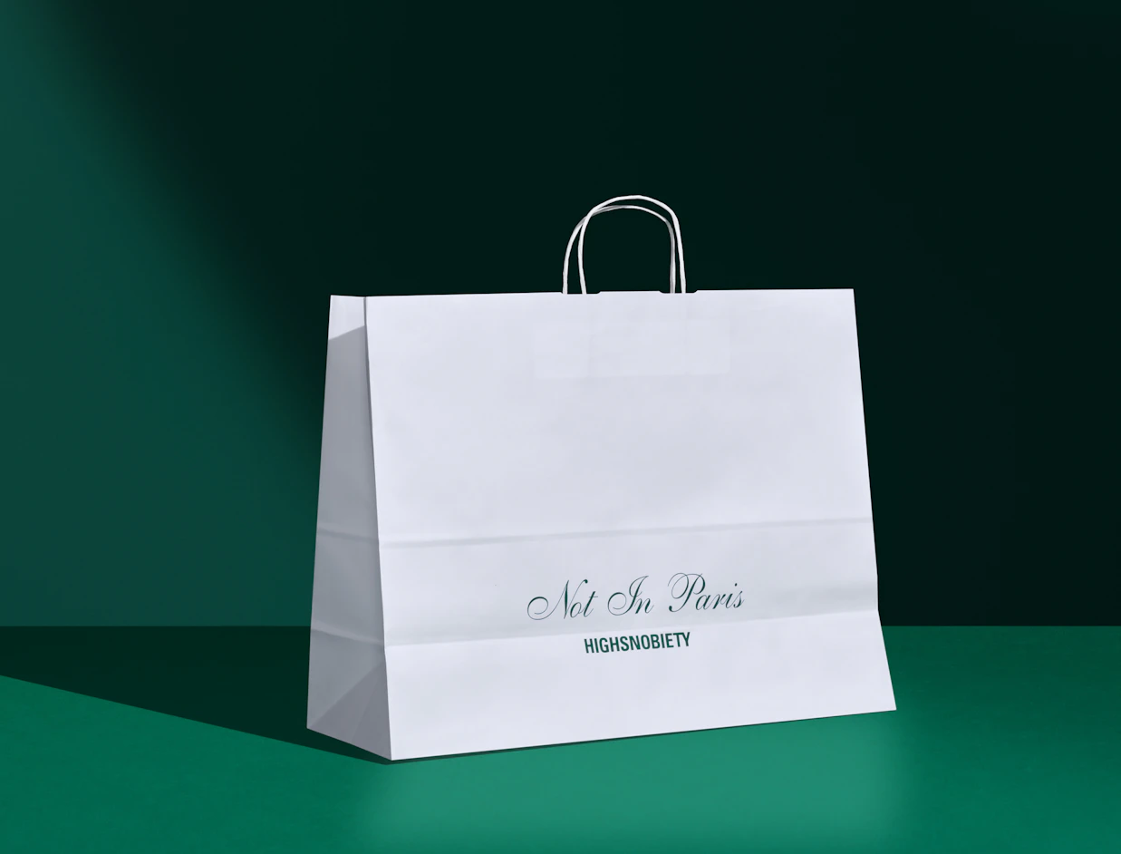 White printed paper bag with twisted handles and a green logo print on a dark green backdrop