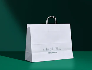 White printed paper bag with twisted handles and a green logo print on a dark green backdrop