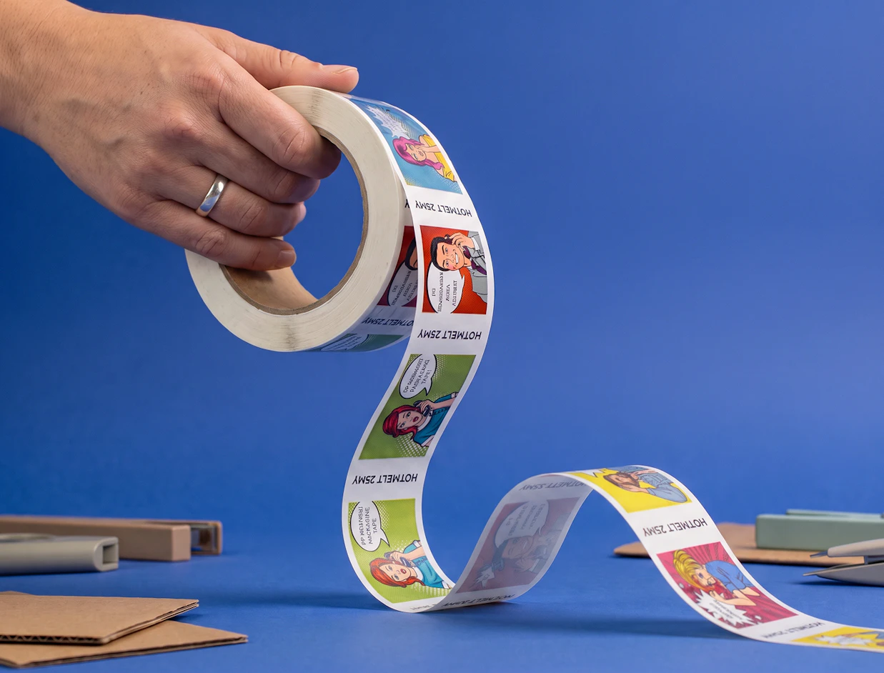A hand unrolling custom tape printed with colorful pop-art comic strip illustrations on a blue background