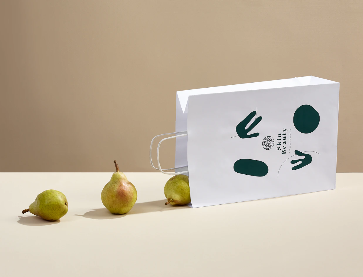 White printed paper bag with a dark green graphic print lying beside pears