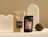 Two 'RAW ORGANIC CACOA MIX' pouches in kraft brown and matte black set against cream geometric props with a whole coconut