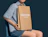 Person seated holding an expandable kraft mailer with a white logo print