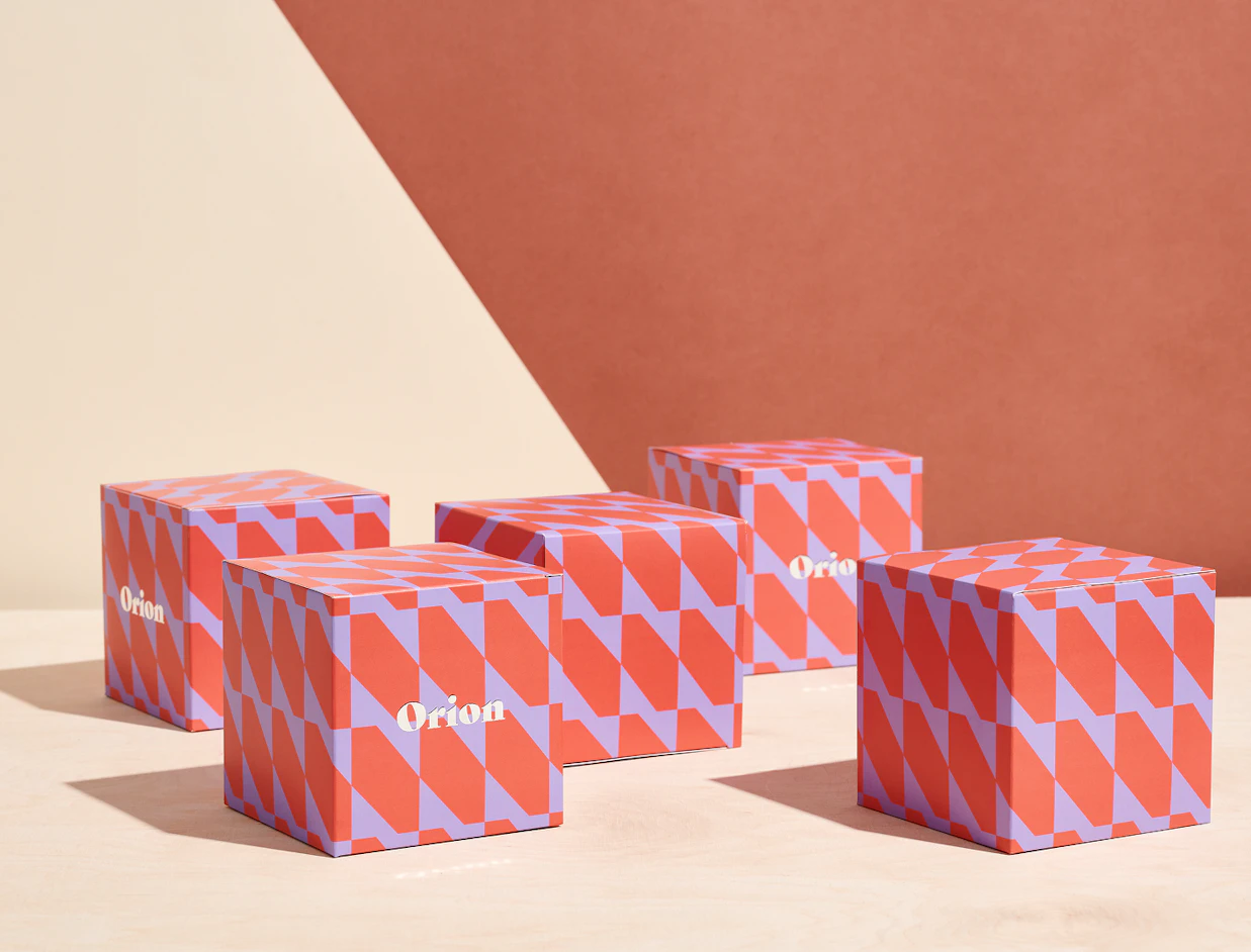 Five red and purple patterned square boxes labeled 'Orion' arranged on a light wood table