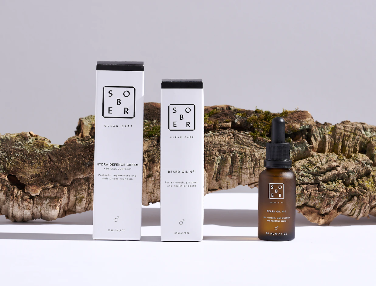 Sober brand skincare products, including Hydra Defence Cream box, Beard Oil box, and a dropper bottle of Beard Oil, set against tree bark