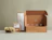 Kraft mailer boxes with white print, one open to show the printed interior, on a sage backdrop