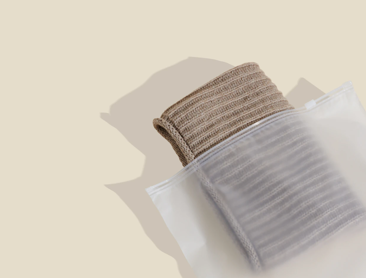 Frosted zipper bag holding a folded grey knit item on a beige background