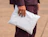 A person in a dark outfit holding a plain white poly mailer bag against a neutral background