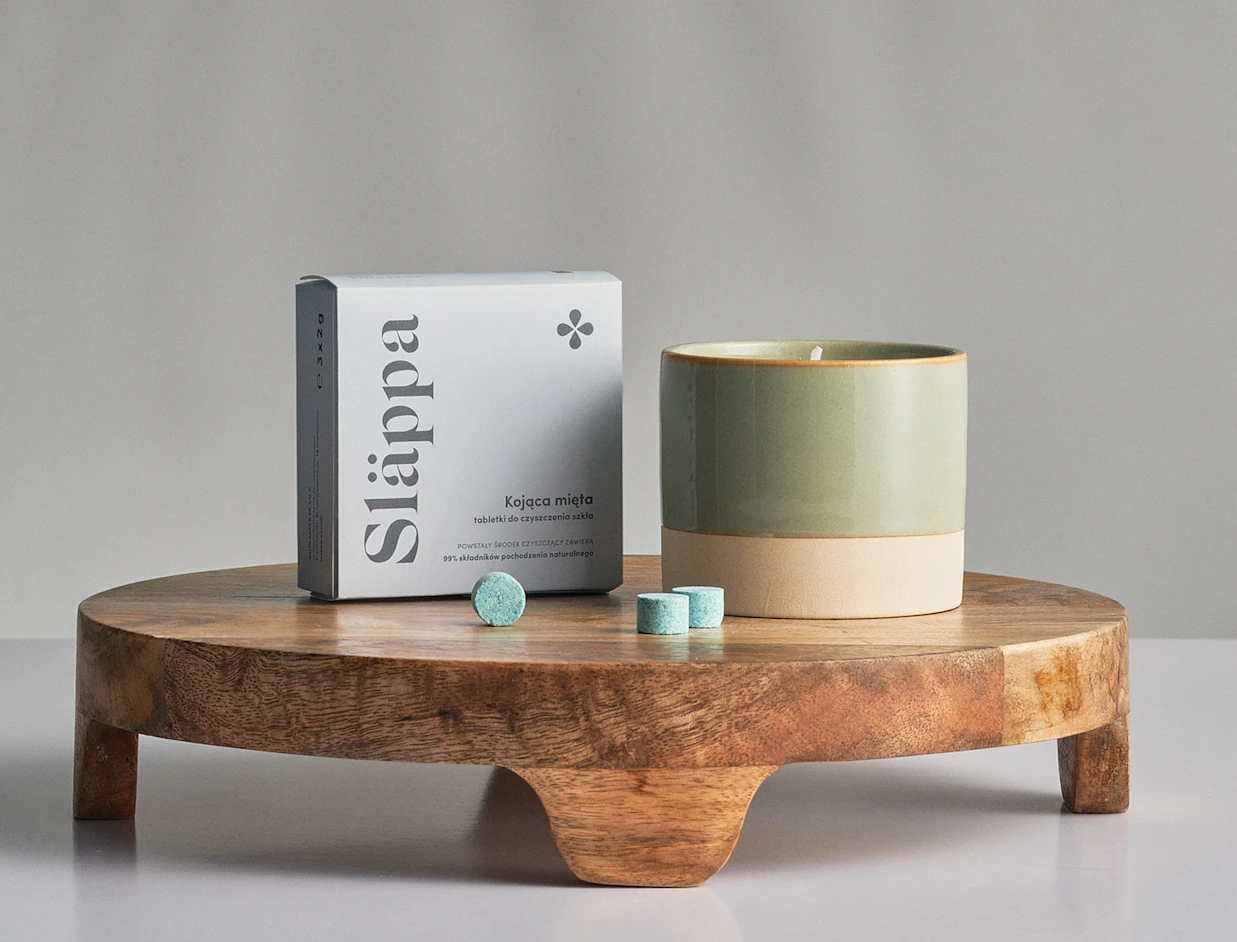 Grey printed product box beside a candle and blue tablets on a wooden stand