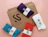 A brown cardboard envelope branded 'SOCIAL SOCKS' surrounded by four pairs of colorful socks in blue, red, purple, and white