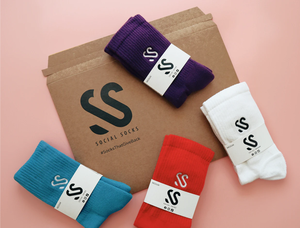 A brown cardboard envelope branded 'SOCIAL SOCKS' surrounded by four pairs of colorful socks in blue, red, purple, and white