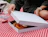 Hands opening a plain white cardboard pizza box revealing a fresh pizza on a red and white checkered picnic blanket