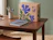 A kraft cardboard box printed with blue floral illustrations and the 'PIXEL AGENCY' logo standing on a wooden desk next to stationery