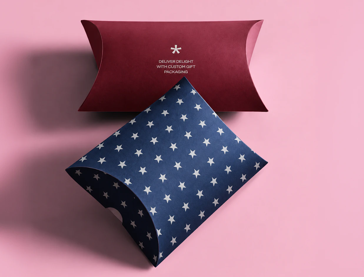 Top-down view of two pillow boxes, one dark red and one blue with a white star pattern, on a pink background