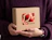 Hands holding a kraft cardboard box embellished with a shiny red metallic foil 'Linoã' logo, set against a dark purple sweater
