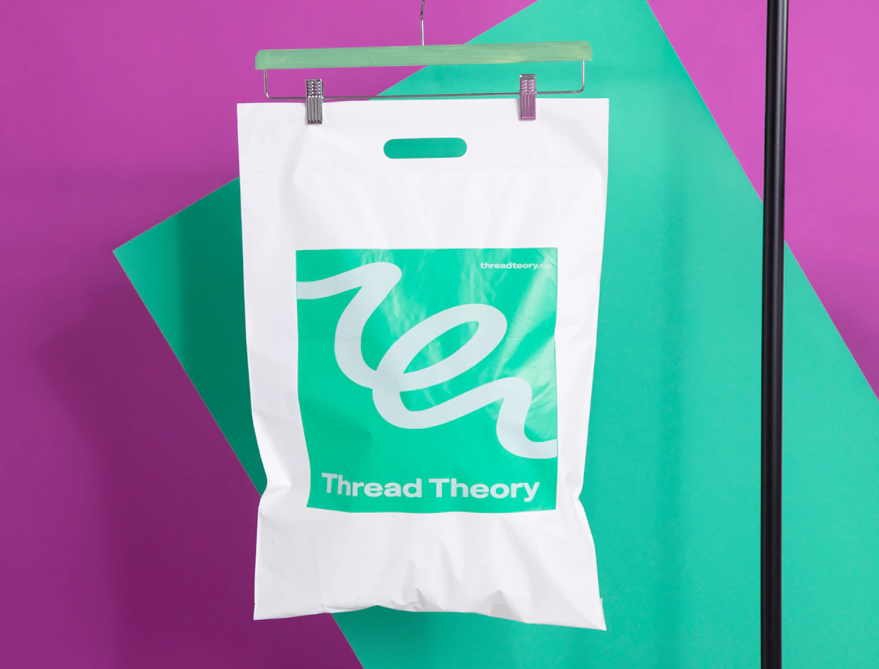White bio poly mailer with a green print and die-cut handle hanging on a rail