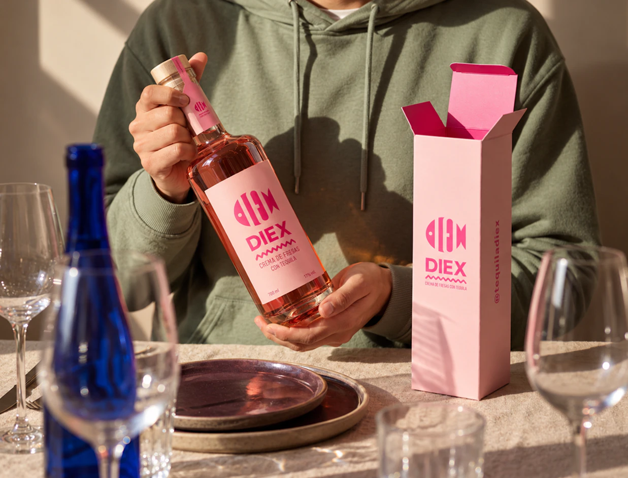 A person in a hoodie holding a bottle of pink tequila cream next to an open matching pink box branded 'DIEX'