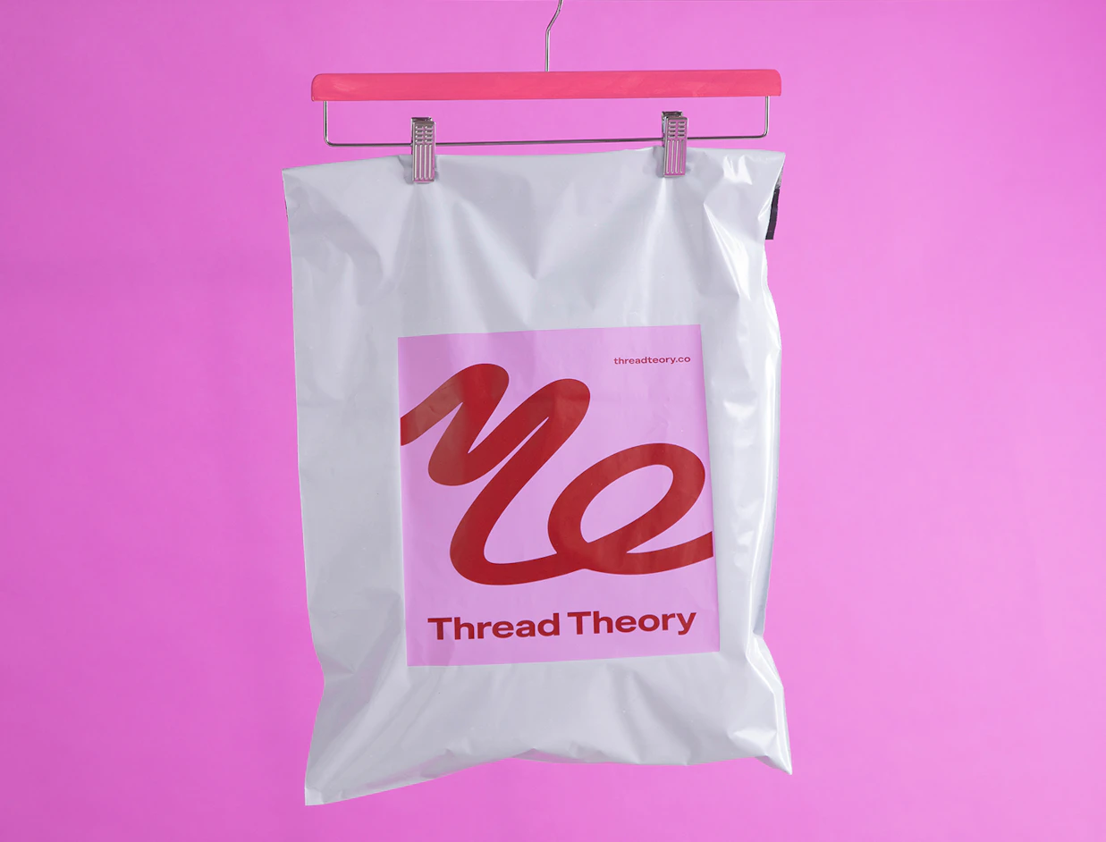 White poly mailer with a pink square logo for Thread Theory hanging on a pink hanger against a vibrant pink background