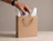A hand placing a wrapped gift into a plain kraft paper bag lined with patterned tissue paper
