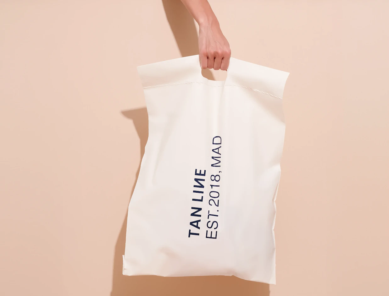 Hand holding a white bio poly mailer with a black text print and die-cut handle