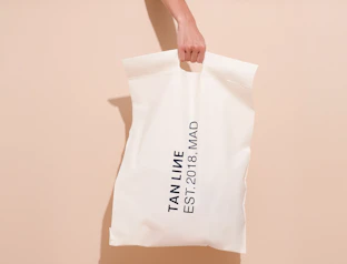 Hand holding a white bio poly mailer with a black text print and die-cut handle