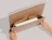 Hands holding open a cardboard book mailer showing books tucked inside internal flaps, printed with 'FOLD IT HOW YOU NEED IT'