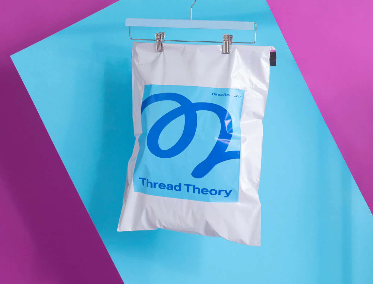 A white poly mailer printed with a blue logo and 'Thread Theory' hanging from a clothes hanger against a blue and purple background