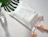Hands peeling the red protective strip off a white bio poly mailer bag printed with sustainability icons, placed next to a monstera leaf