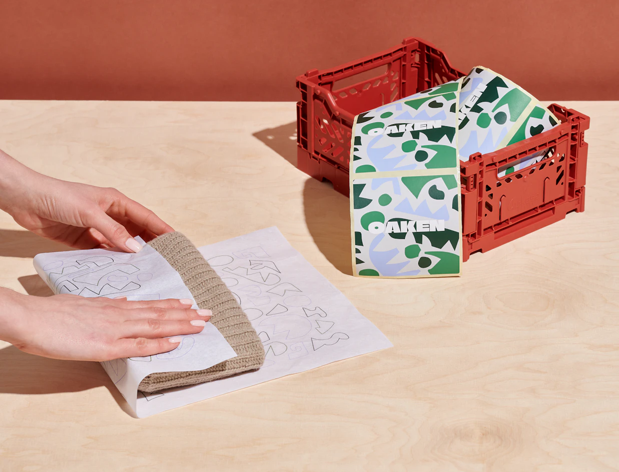 Hands wrapping an item in custom printed white tissue paper beside an open red crate