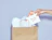 A hand pulling a white 'thank you!' card out of a brown paper shopping bag filled with tissue paper