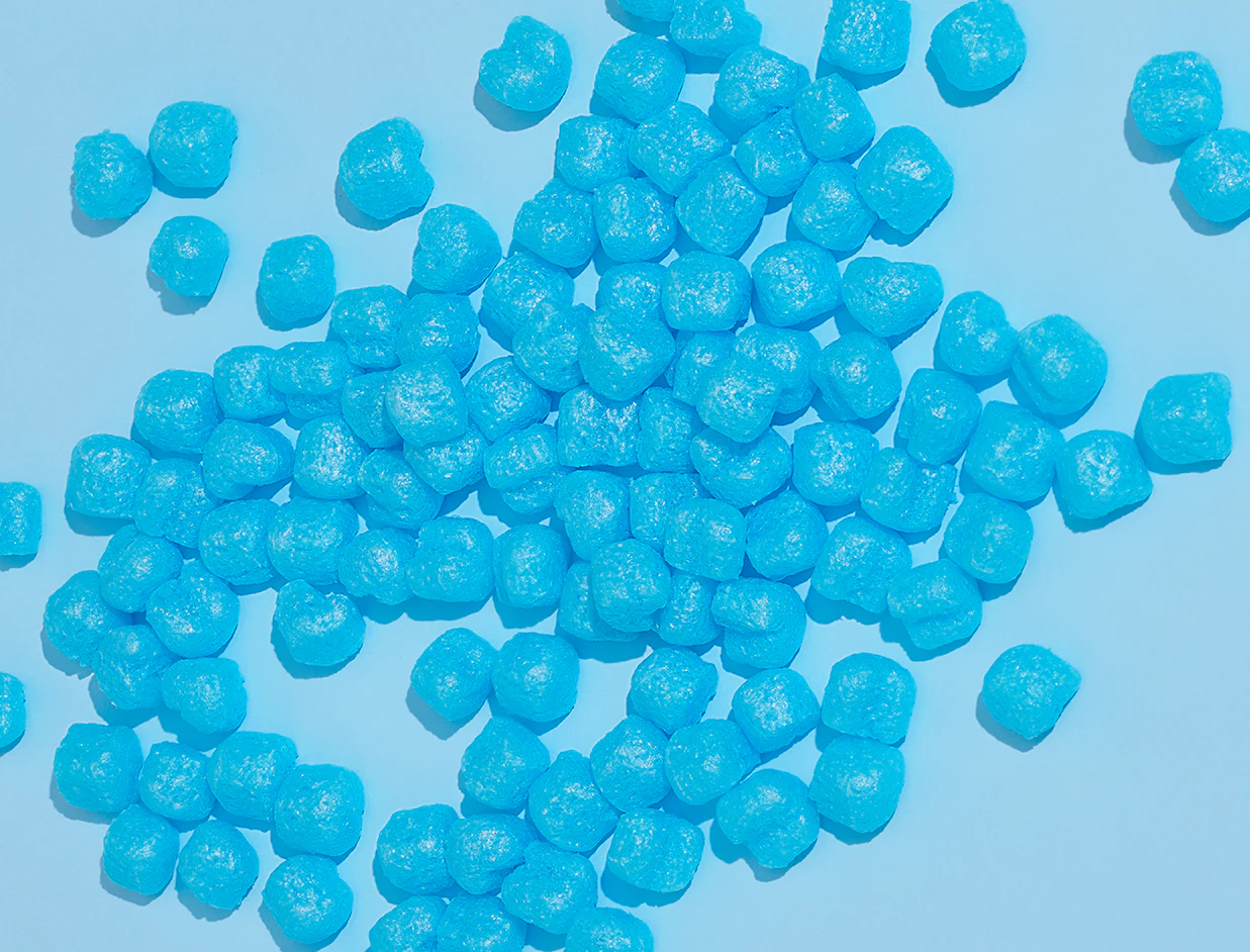 Top-down view of bright blue biodegradable foam packing peanuts scattered across a light blue background