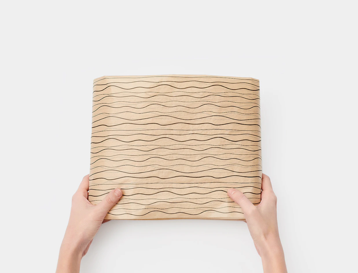 Top-down view of hands holding a item neatly wrapped in brown tissue paper printed with black wavy lines