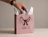 A hand placing a wrapped item into a dusky pink paper gift bag branded 'ARCII' with black rope handles