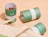 Green and white printed paper cans, one open with loose tea, beside a cotton bag