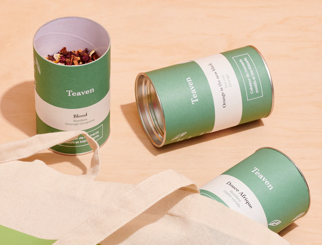 Green and white printed paper cans, one open with loose tea, beside a cotton bag