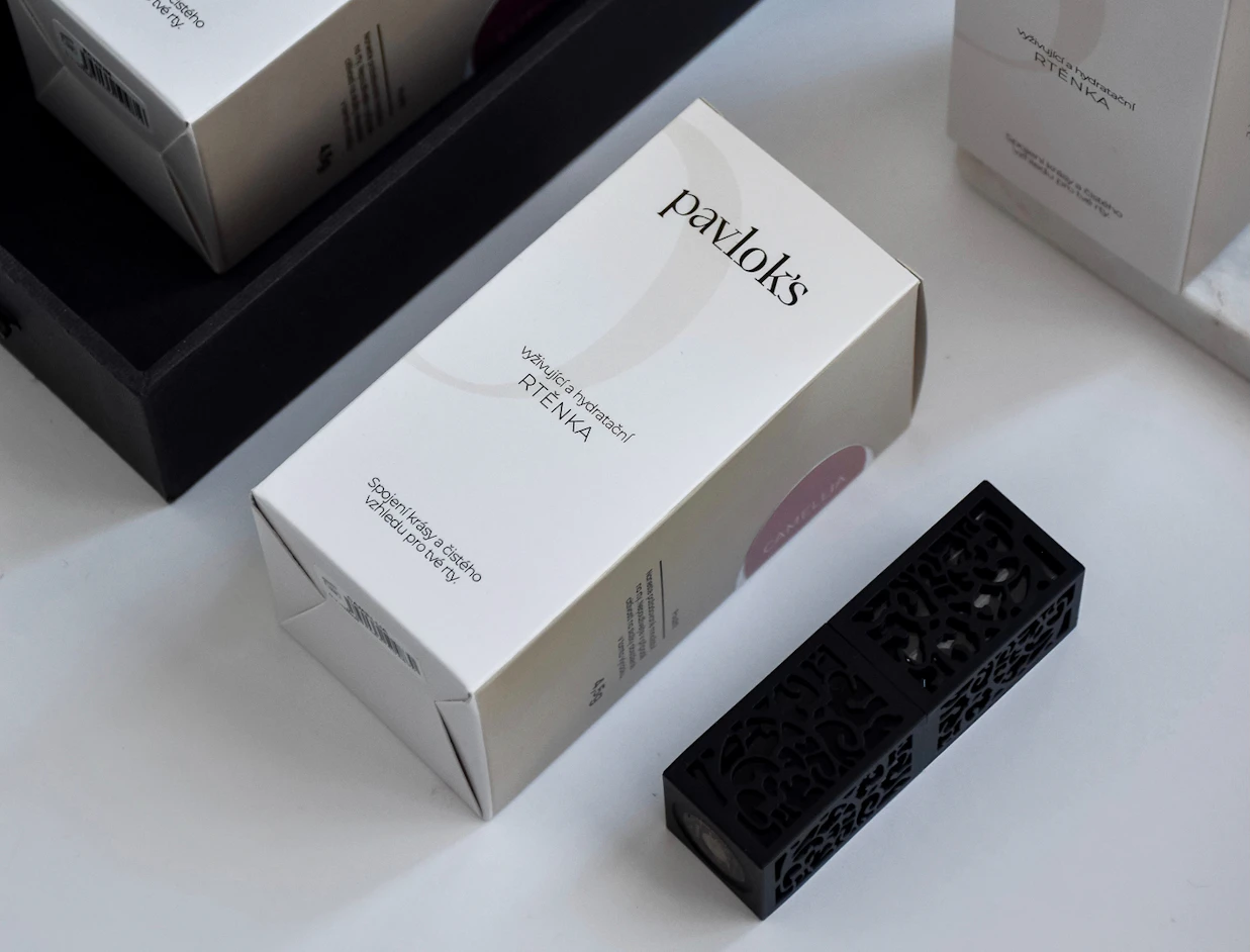 A white pavlok's cosmetics box alongside a black carved lipstick case on a bright surface