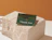 A green 'Thank You for your order' card resting on a stone display block next to a gold pendant necklace