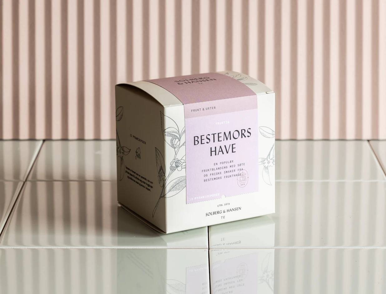White product box with a botanical print and lilac label on a tiled surface