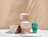 Three cardboard POLŪ product boxes stacked next to a teal reusable coffee cup on a white table