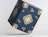 Dark blue cube product box decorated with intricate gold floral and snowflake patterns, tilted against a white background