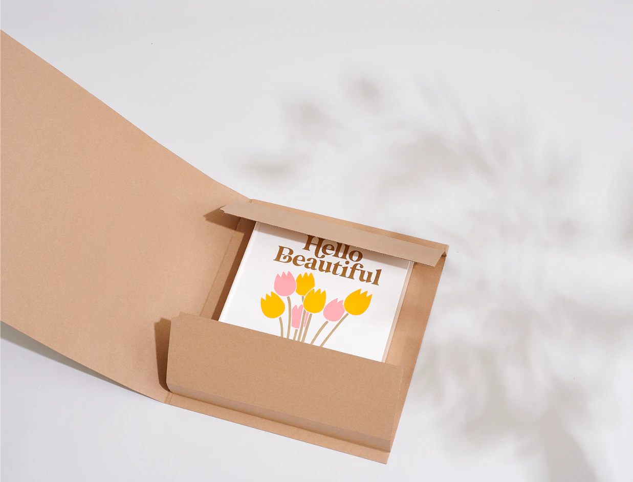 An open kraft cardboard book mailer displaying a book titled 'Hello Beautiful' with colorful tulip graphics inside
