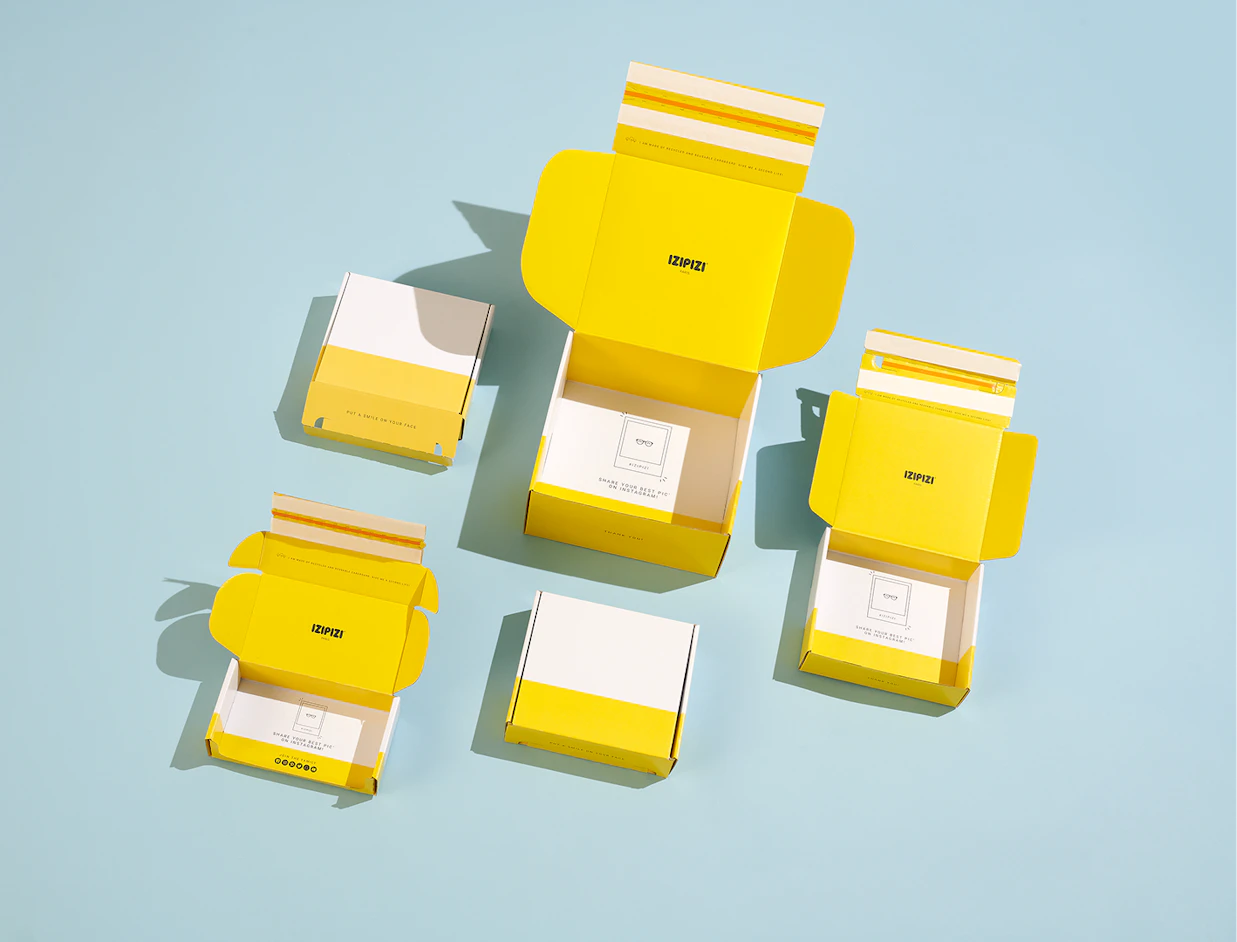 An assortment of open and closed white and bright yellow mailer boxes branded 'IZIPIZI' displayed on a light blue background