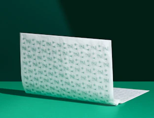 White tissue paper sheet with a repeating green logo pattern, standing on a green surface