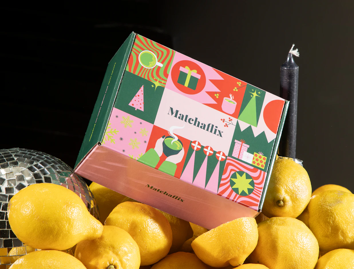 Full colour mailer box with a vivid multicolour festive pattern, resting on lemons